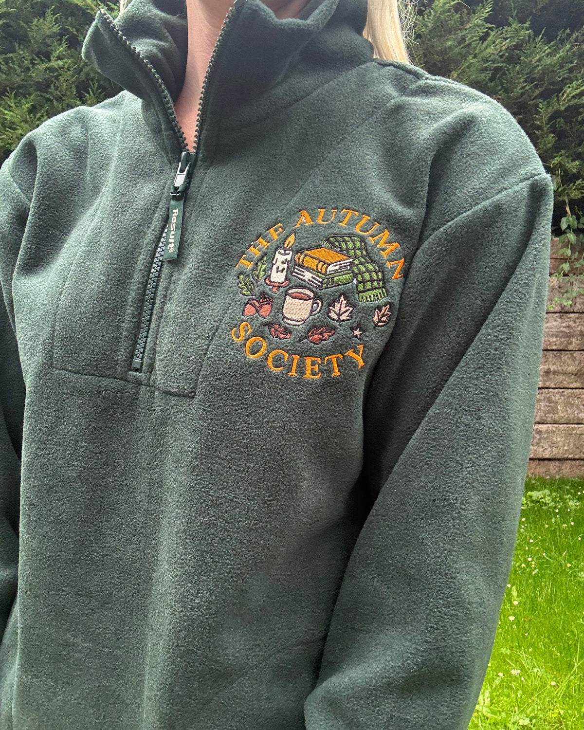 Forest green embroidered quarter zip fleece featuring The Autumn Society autumn design with books, candle, mug and autumn leaves on the chest.